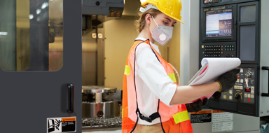 A female supervisor/operator in a factory is checking on a terminal of milling machine