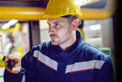 Male engineer wearing a hard hat and inspecting pipework inside a factory