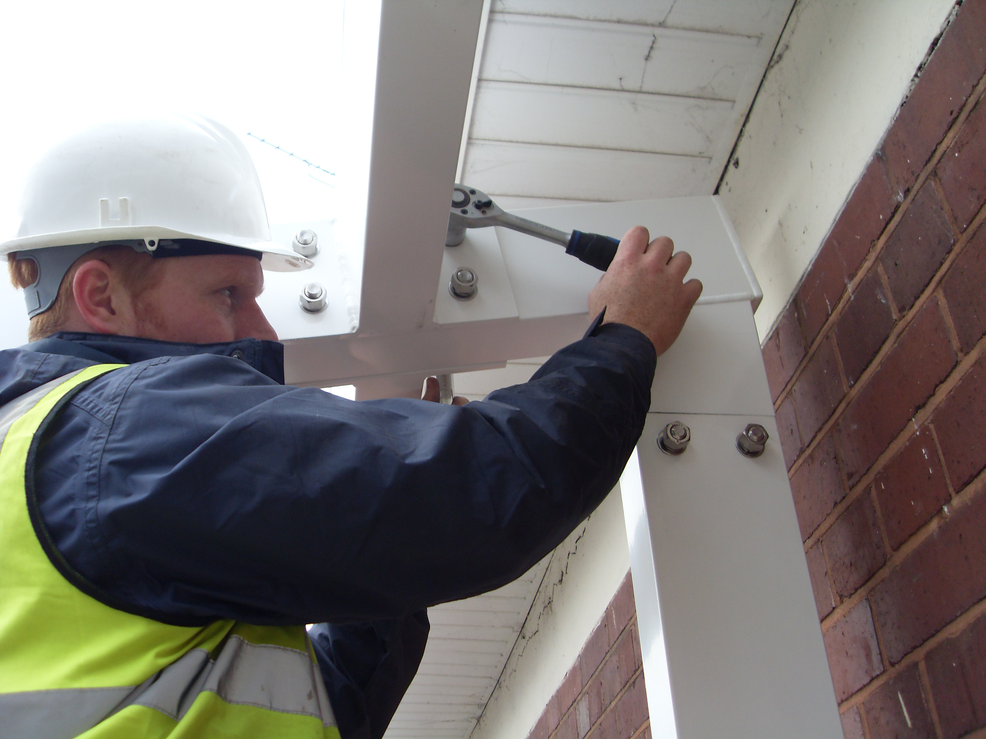Twinfix staff member in a hard hat tightening bolts on a building