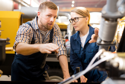 One of young confident technicians pointing at mechanism of industrial equipment during discussion of its qualities with colleague