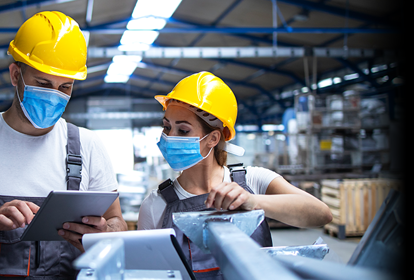 Industrial workers with face masks protected against corona virus discussing about production in factory. People working during COVID-19 pandemic