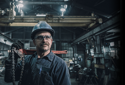 Male worker carrying work tool looking away while standing in factory