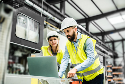 A portrait of a mature industrial man and woman engineer with laptop in a factory, working.