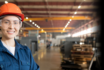 Young smiling female technician in blue uniform, protective eyeglasses and helmet working in modern factory