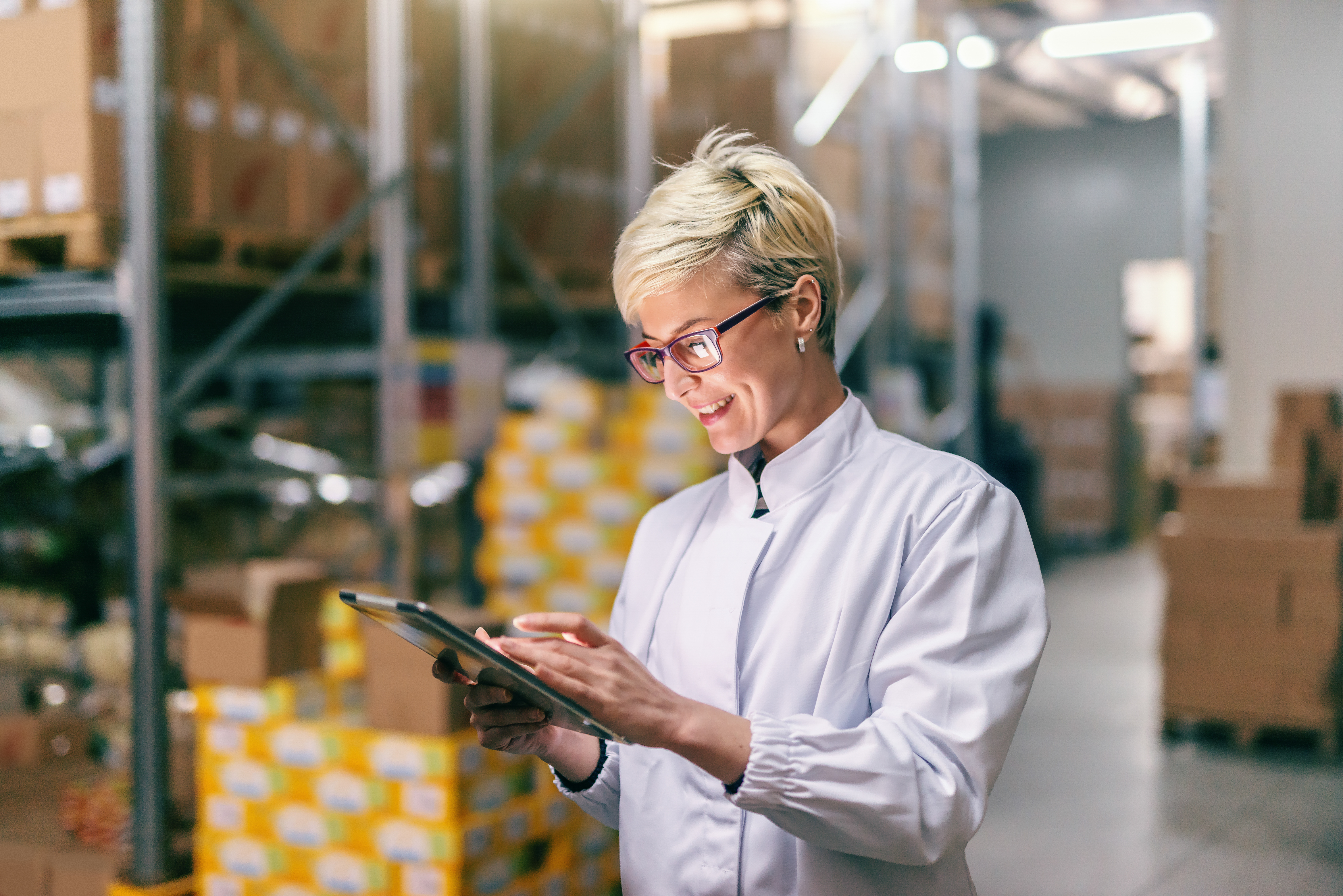 Blonde woman in white uniform using tablet in warehouse