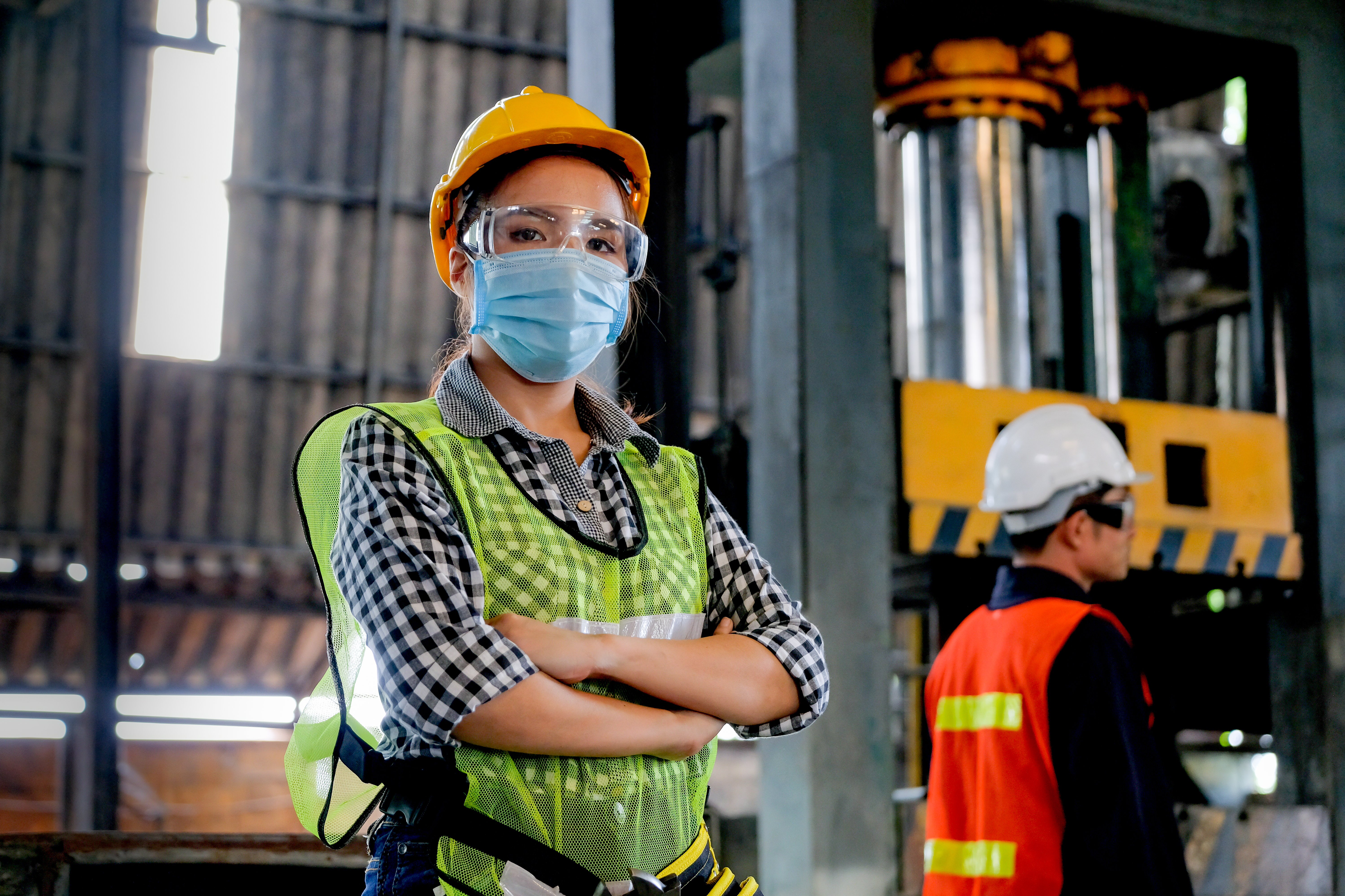 Factory woman worker or technician with hygienic mask stand with confident action with her co-worker as background.